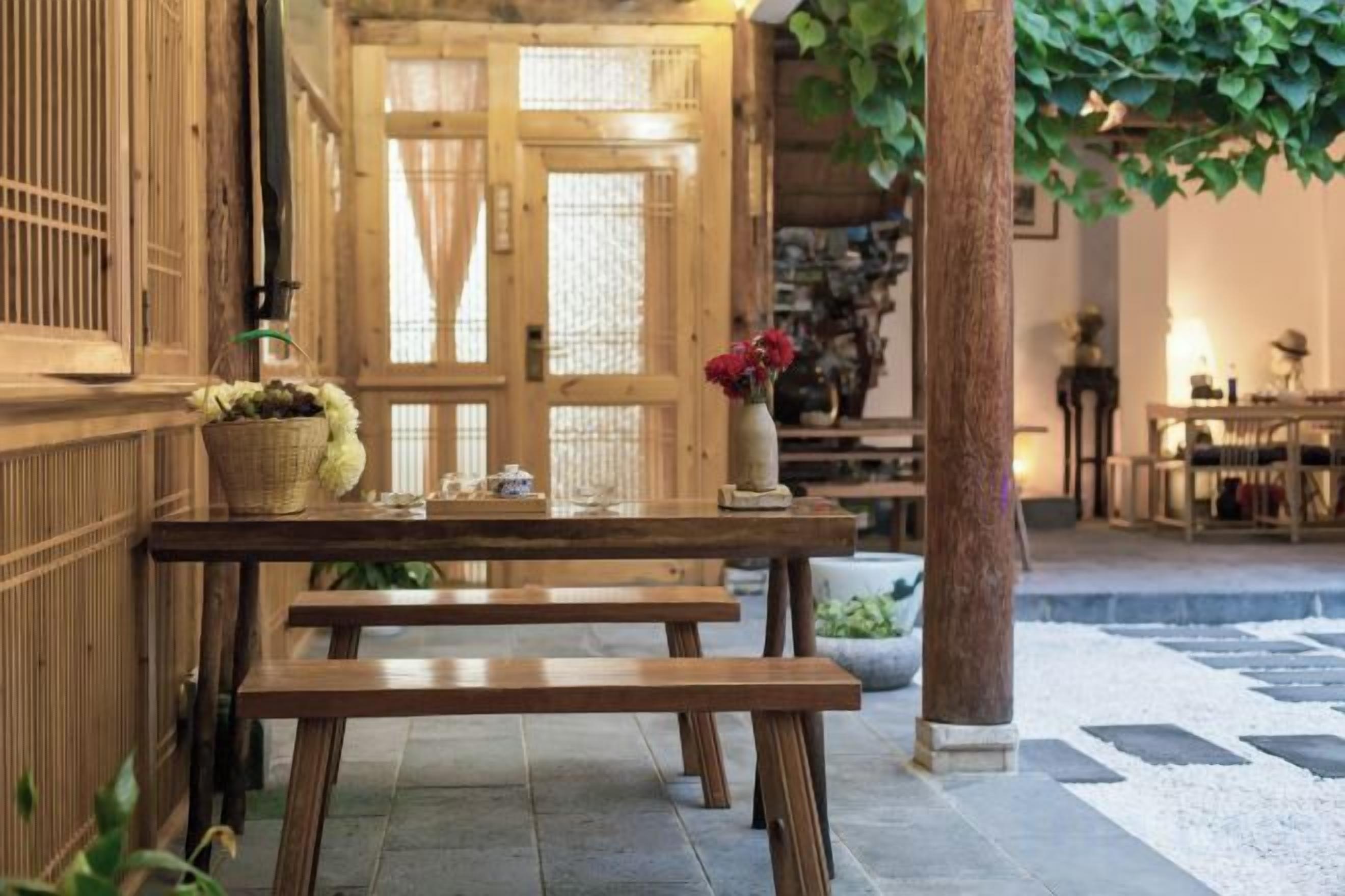 A wooden bench and table set in a traditional interior with a tiled floor and a wooden door in the background.
