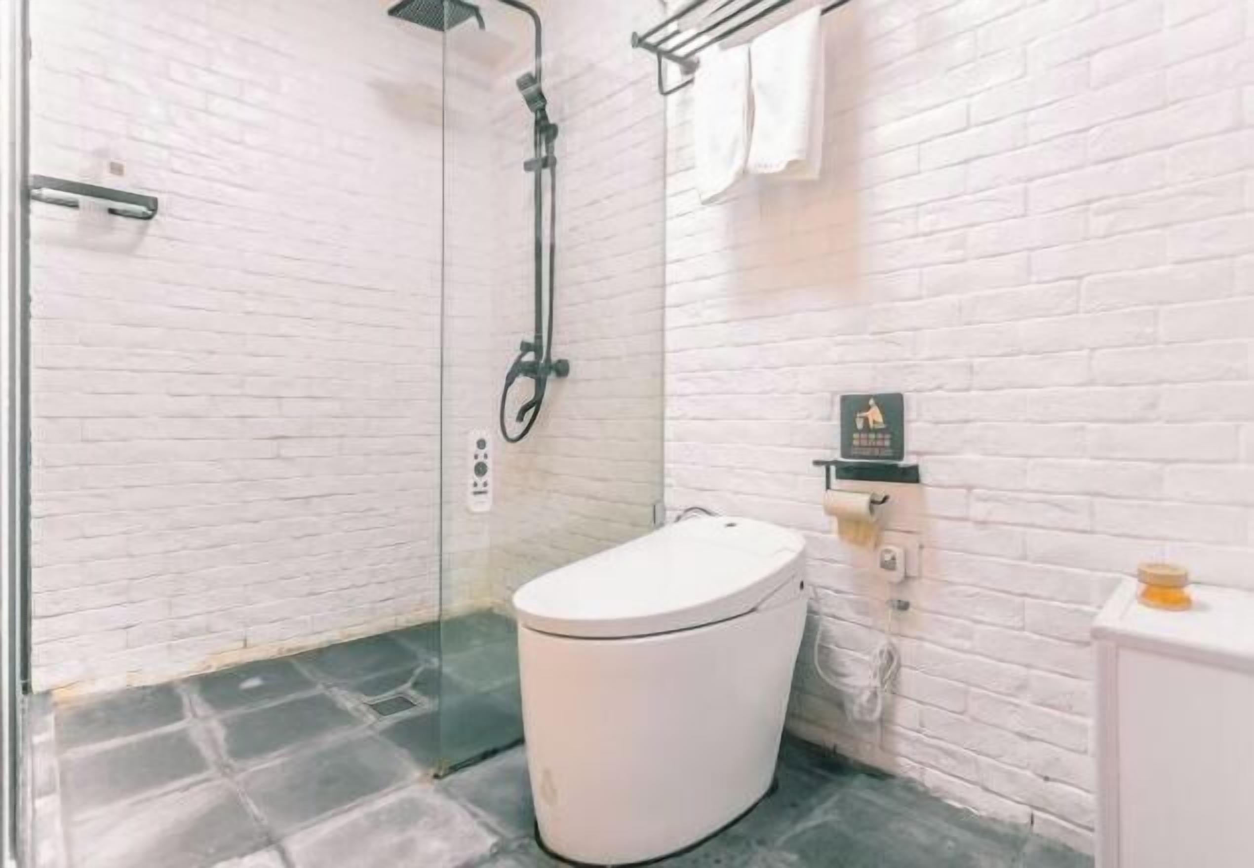 Ein Badezimmer mit Toilette, Duschkabine aus Glas und einer Wand aus weißen Ziegelsteinen.