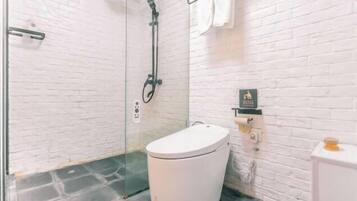 Ein Badezimmer mit Toilette, Duschkabine aus Glas und einer Wand aus weißen Ziegelsteinen.