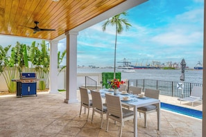 An outdoor patio with a dining table, chairs, a grill, and a view of the water and port. - Million Dollar Views / Private beach / Heated pool / Walk to Beach / Harbourview Key | VlLLAS (Fort Lauderdale)