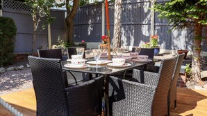 An outdoor patio with a glass-top table surrounded by wicker chairs, set against a wooden deck. - 13 The Crescent (Colwyn Bay)