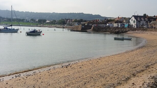 A coastal scene with boats on calm water, a sandy beach, and buildings in the background. - 13 The Crescent (Colwyn Bay)