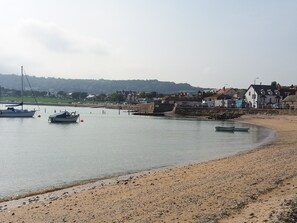 A coastal scene with boats on calm water, a sandy beach, and buildings in the background. - 13 The Crescent (Colwyn Bay)