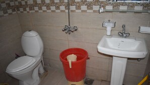 A bathroom with a toilet, a red bucket, and a sink. - Hotel 1947 (Gilgit)