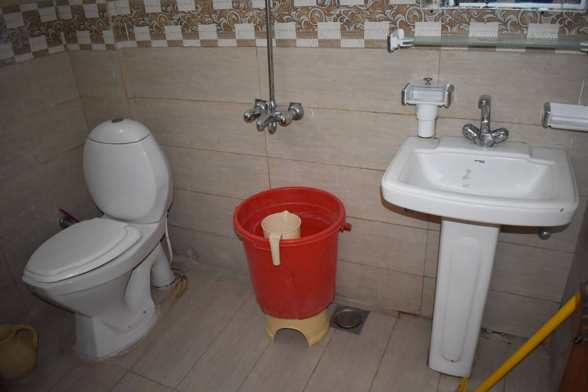 A bathroom with a toilet, a red bucket, and a sink.