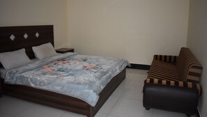 A bedroom with a bed, a nightstand, and a striped sofa. - Hotel 1947 (Gilgit)