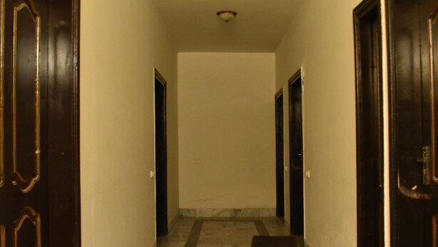 A hallway with dark wooden doors, white walls, and a marble floor. - Hotel 1947 (Gilgit)