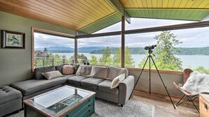 Ein modernes Wohnzimmer mit großem Fenster, einer Couch, einem Glastisch und einem Stativ.