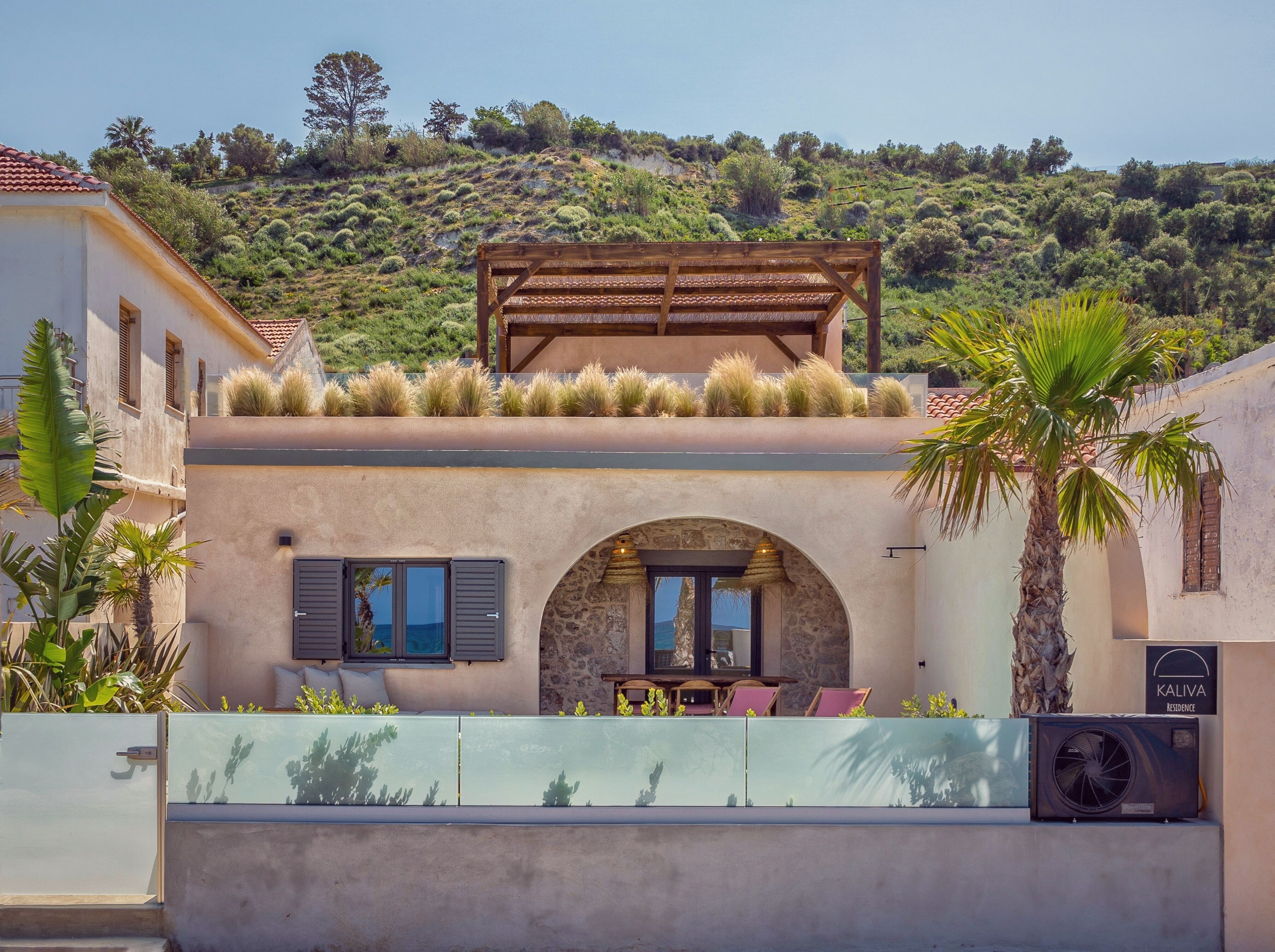 A Mediterranean-style villa with a stone archway entrance, outdoor seating, and a view of a hillside.