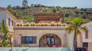 A Mediterranean-style villa with a stone archway entrance, outdoor seating, and a view of a hillside. - Kaliva Residence (Apokoronas)