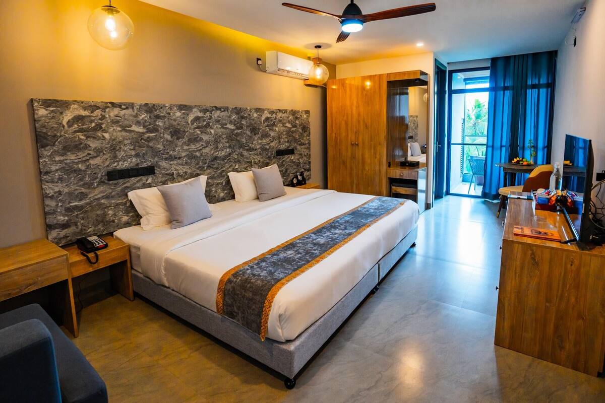 A modern hotel room with a large bed, a desk, a wardrobe, and a view of the outdoors.