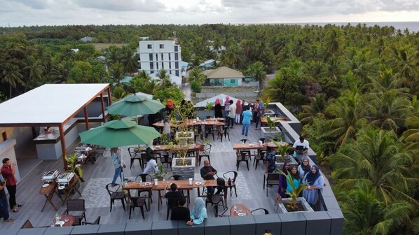 An outdoor dining area with tables and chairs, surrounded by lush greenery and palm trees.