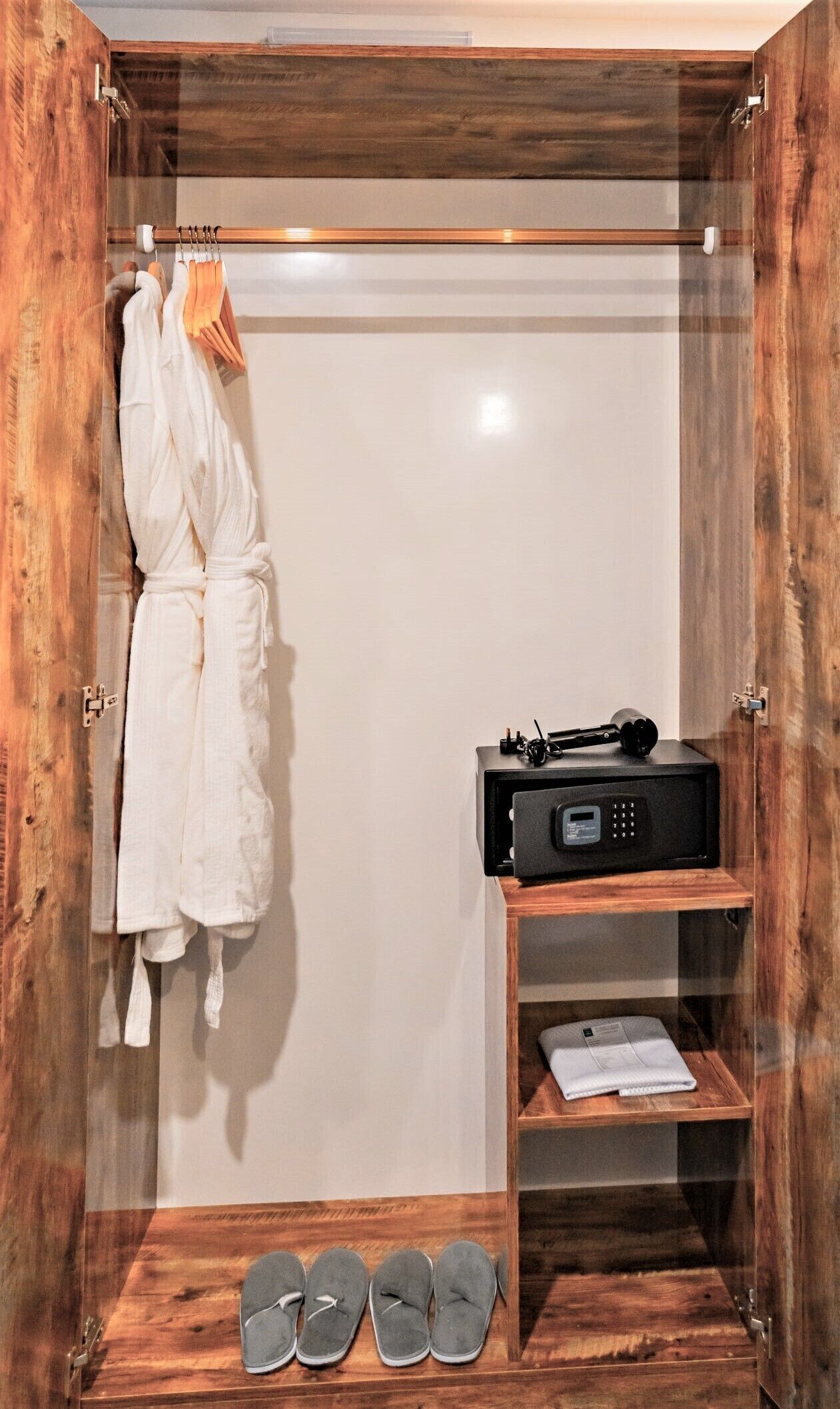 A walk-in closet with a wooden door, a robe hanging on a rack, a black radio, and a pair of slippers on the floor.
