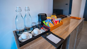 A hotel room with a wooden desk, two glass bottles, a coffee maker, snacks, a tray with cups and saucers, and a TV. - Maa Thundi (Fuvahmulah)