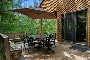 A wooden deck with a table and chairs, an umbrella, and a sliding glass door. - Trout Creek Resort/Golf/Beaches/Pools/Hot tub/Sauna/Pet friendly (Harbor Springs)