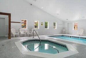 A spacious indoor swimming pool with a small hot tub, surrounded by white chairs and a tiled border. - Trout Creek Resort/Golf/Beaches/Pools/Hot tub/Sauna/Pet friendly (Harbor Springs)
