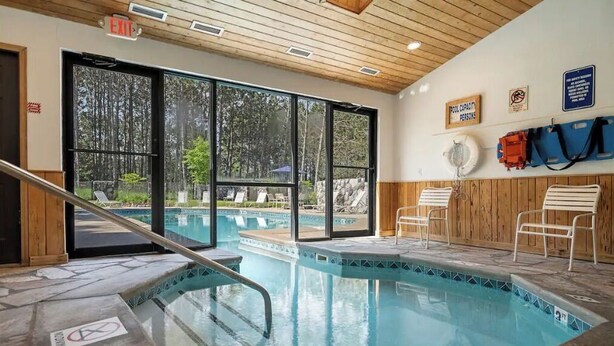 Una piscina interior con techo de madera, ventanas amplias y vistas al exterior.