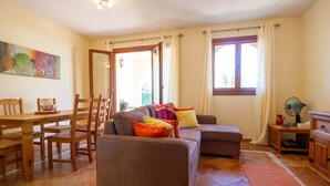 A living room with a sofa, chairs, a dining table, and a window with curtains.