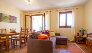 Een woonkamer met een bank, stoelen, een eettafel en een raam met gordijnen.