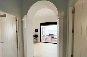 A hallway with white walls and a tiled floor leading to a balcony with a table and chairs.