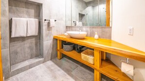 Ein modernes Badezimmer mit einem Holzkosmetikschrank, einem großen Spiegel und einer bodenebenen Dusche.