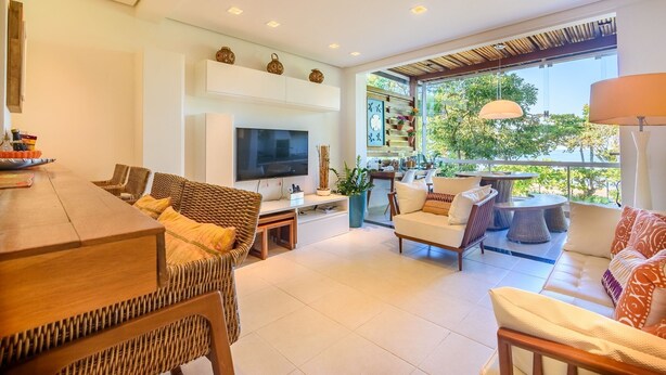A spacious living room with a large TV, comfortable seating, a dining area, and a view of the outdoors. - Pé na areia com charme e elegância (São Sebastião)