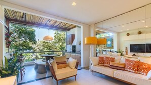 A spacious living area with a sofa, chairs, and a dining table. There is a balcony with plants and a view of greenery. - Pé na areia com charme e elegância (São Sebastião)