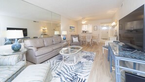 A modern living room with a sofa, a glass coffee table, and a dining area with chairs and a table.