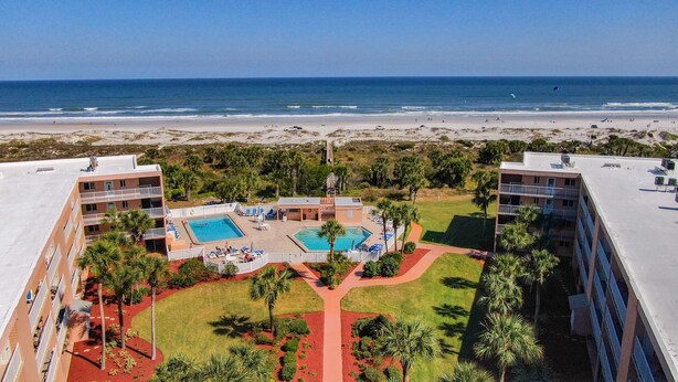 A hotel with a pool area, surrounded by palm trees and a view of the beach.