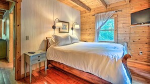 Een slaapkamer met houten lambrisering, een bed, bedlampen, een televisie en een raam met gordijnen.