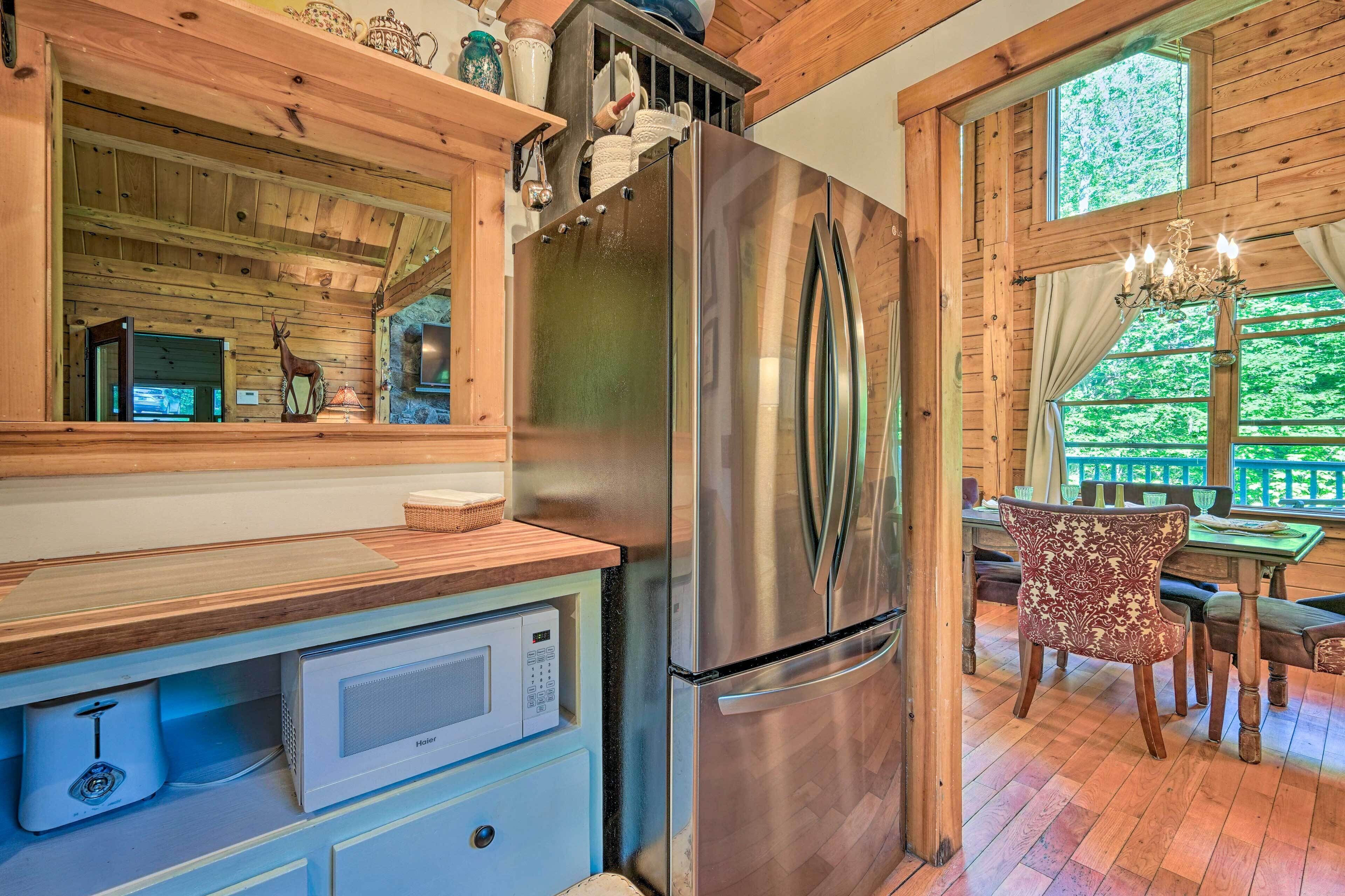 A modern kitchen with a stainless steel refrigerator, wooden cabinetry, a microwave, and a dining area with a table and chairs.