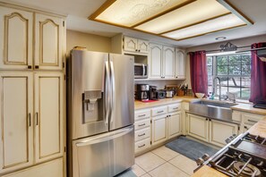A kitchen with a stainless steel refrigerator, microwave, and stove, wooden cabinets, and a window with curtains.