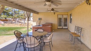 An outdoor patio with a ceiling fan, a table with chairs, a hot tub, and a view of a fenced area with trees. - Spacious Lancaster Family Ranch - BBQ & Patio (Lancaster)