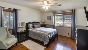A bedroom with a bed, a nightstand, a lamp, a chair, a window with curtains, and a ceiling fan. - Spacious Lancaster Family Ranch - BBQ & Patio (Lancaster)