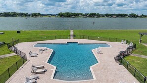 A swimming pool with a unique geometric shape, surrounded by a paved deck with lounge chairs and a fence. - Lakefront Paradise with Stunning Views! (Corsicana)