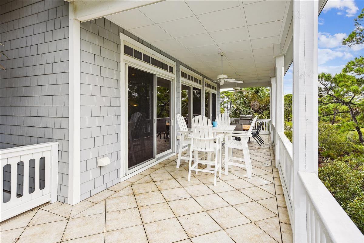 A covered patio with a table and chairs, large windows, and a view of greenery.