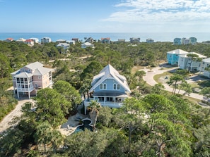 A coastal residential area with multiple houses, a large house with a wrap-around porch, and a view of the ocean. - Let Camelot become your escape from realty. (St. George Island)