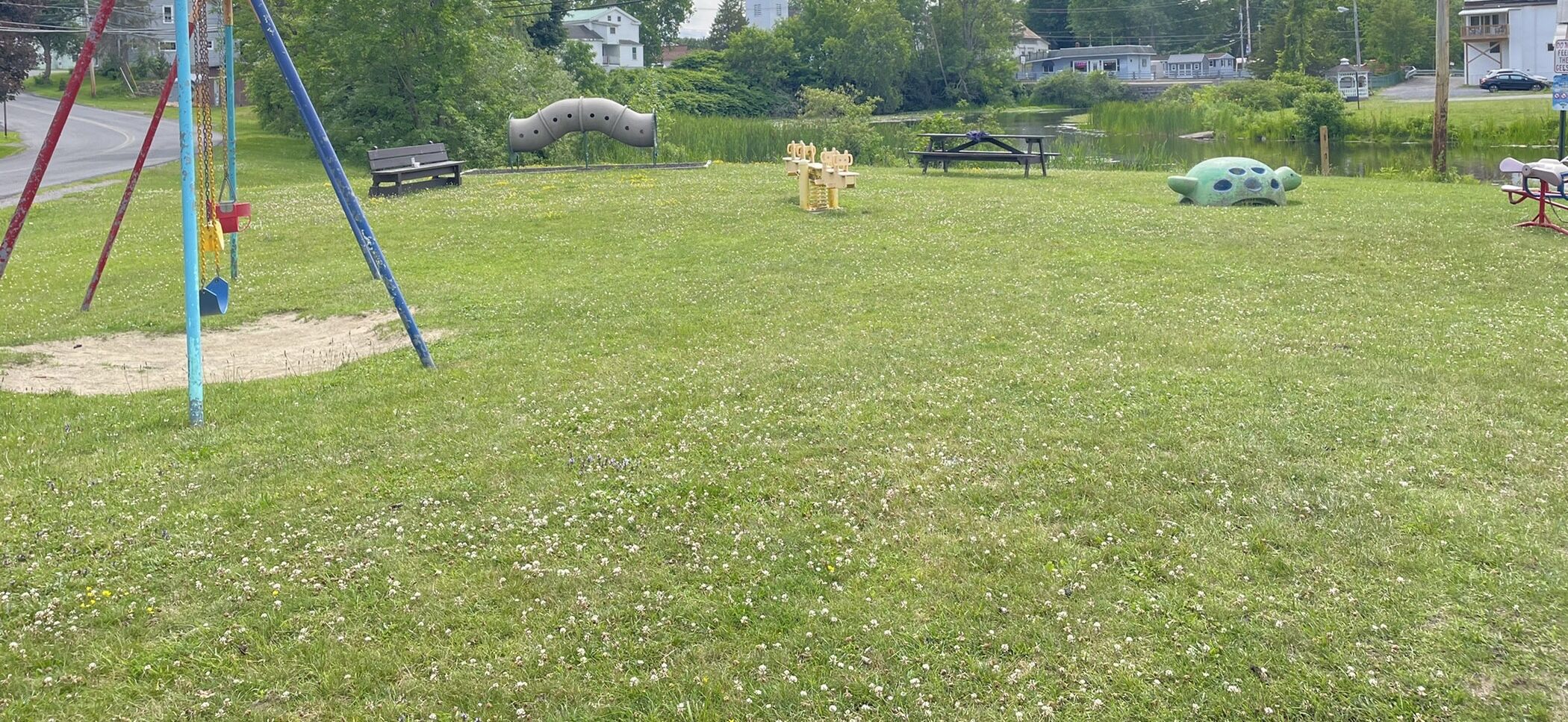 A park with a playground, picnic tables, and a pond.