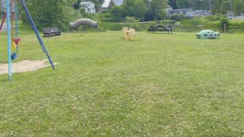 A park with a playground, picnic tables, and a pond.