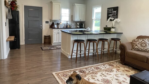 Una cocina moderna con armarios blancos, una isla central con taburetes y un perro acostado sobre una alfombra.