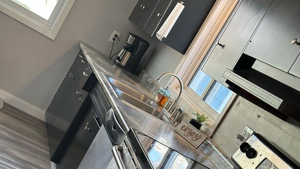 Una cocina moderna con armarios oscuros, electrodomésticos de acero inoxidable y un ventanal que proporciona luz natural.