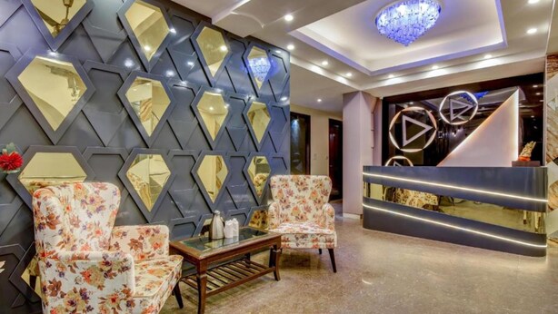 A lobby with a reception desk, two floral armchairs, a coffee table, and a wall with diamond-shaped mirrors. - Staybook Hotel Aira  (New Delhi)
