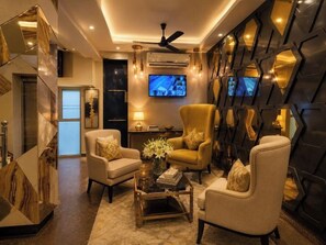 A modern living room with a sofa, armchairs, a coffee table, and a television. - Staybook Hotel Aira  (New Delhi)