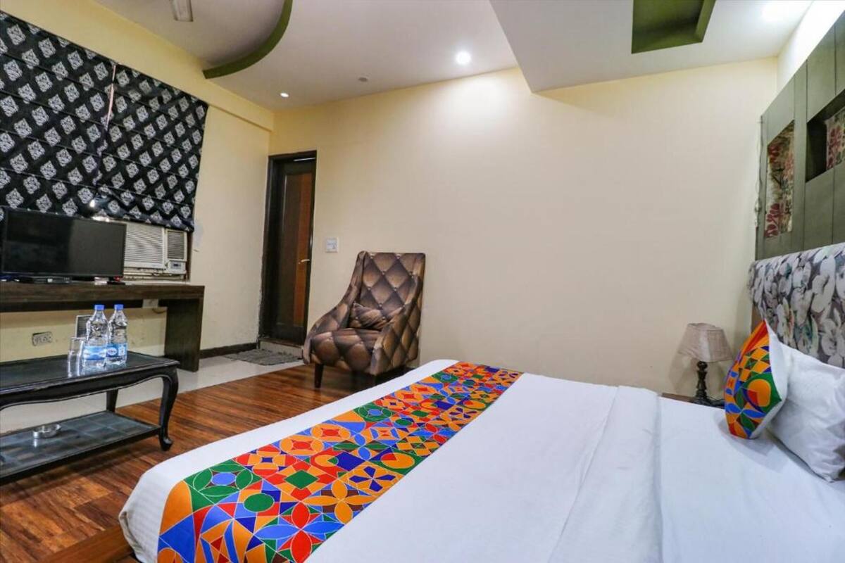 A hotel room with a bed, a chair, a TV, and a table with water bottles.