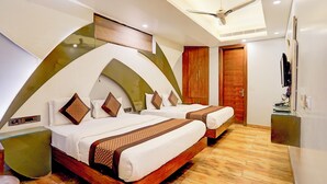 A modern hotel room with two beds, a wooden wardrobe, a ceiling fan, and a television on a stand. - Staybook Hotel Aira  (New Delhi)