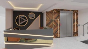 A modern reception area with a reception desk, a wall with geometric patterns, and an elevator. - Staybook Hotel Aira  (New Delhi)