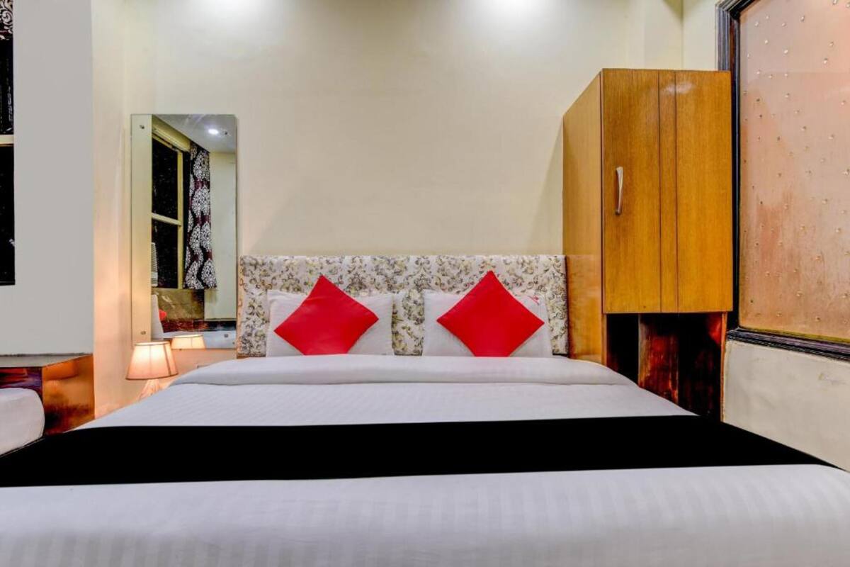 A hotel room with a bed, a wardrobe, a mirror, and a nightstand with a lamp.