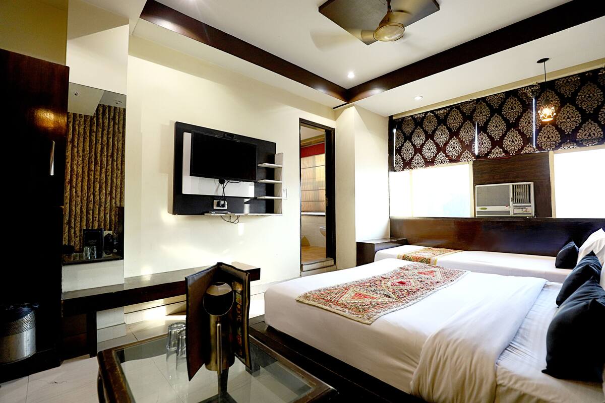 A hotel room with a large bed, a TV mounted on the wall, a desk with a chair, and a patterned wall design.