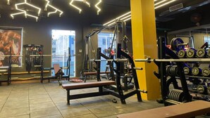 A gym with weightlifting equipment, benches, and a large mirror. - Staybook Hotel Aira  (New Delhi)