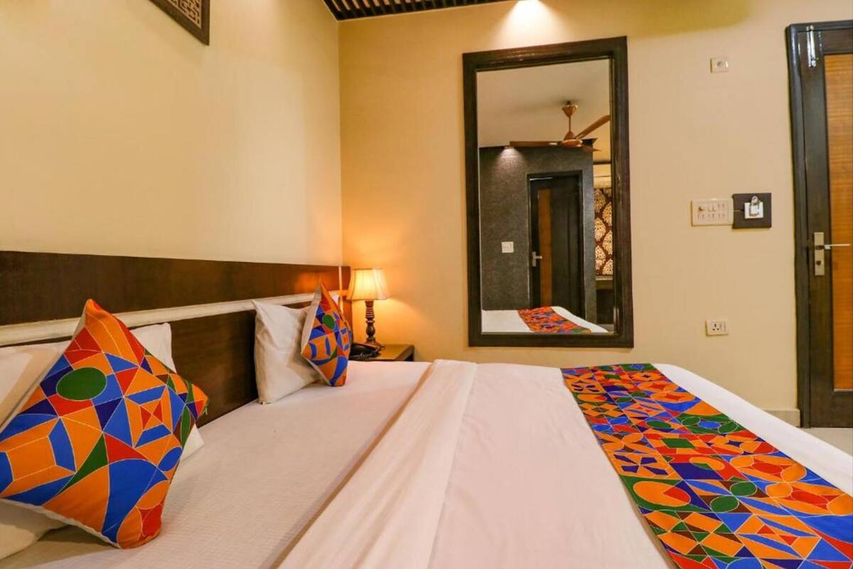A hotel room with a bed, pillows, a nightstand, a lamp, a mirror, and a door.
